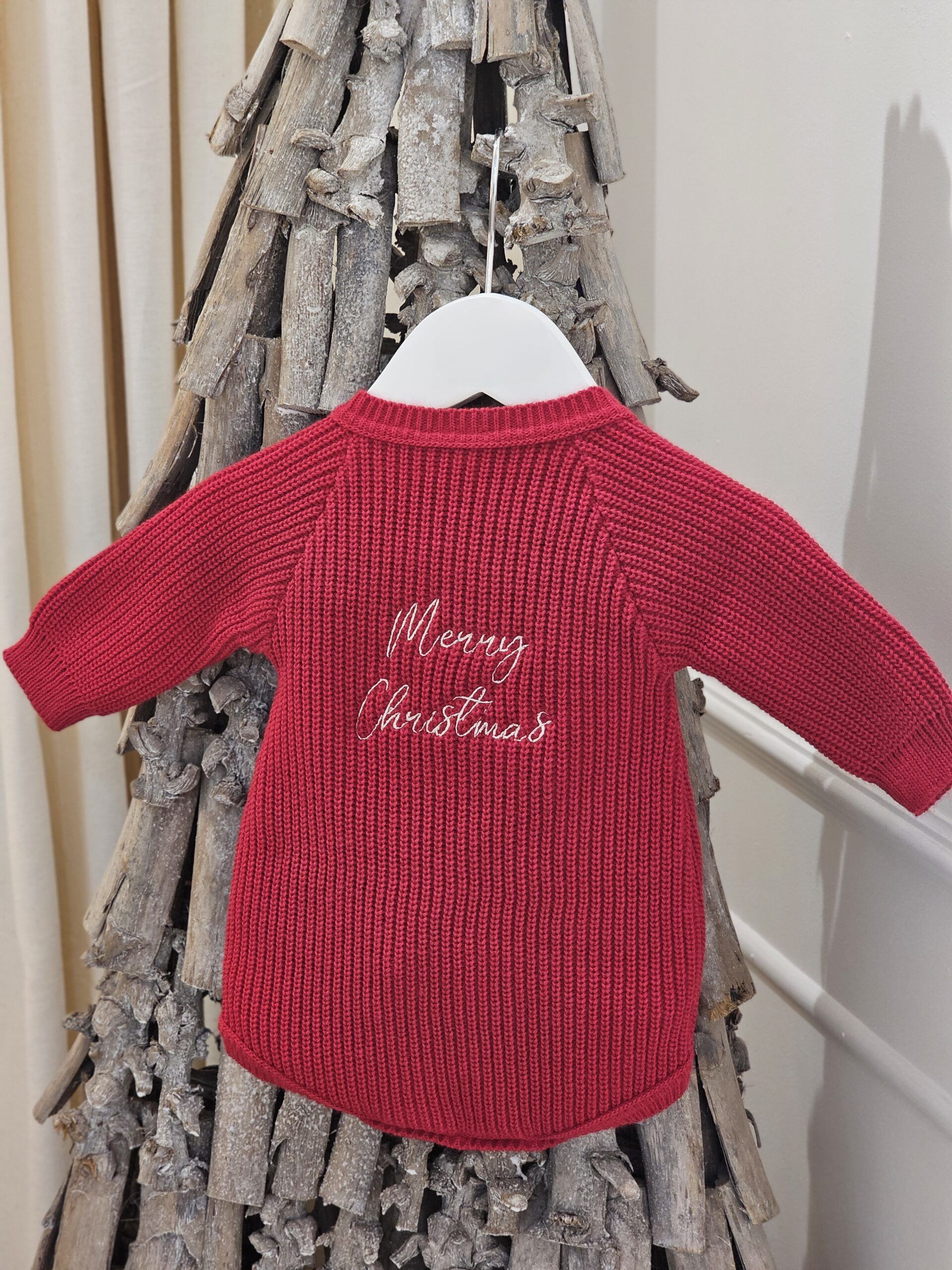 the 'Merry Christmas' Red Romper displayed hanging from a decorative twig tree.