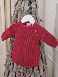 the Dandelion Red Long Sleeve Knitted Romper displayed on a decorative twig tree.