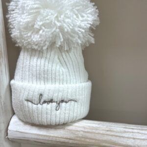 The Baby Store Love You wool pom hat displayed on rustic ladder