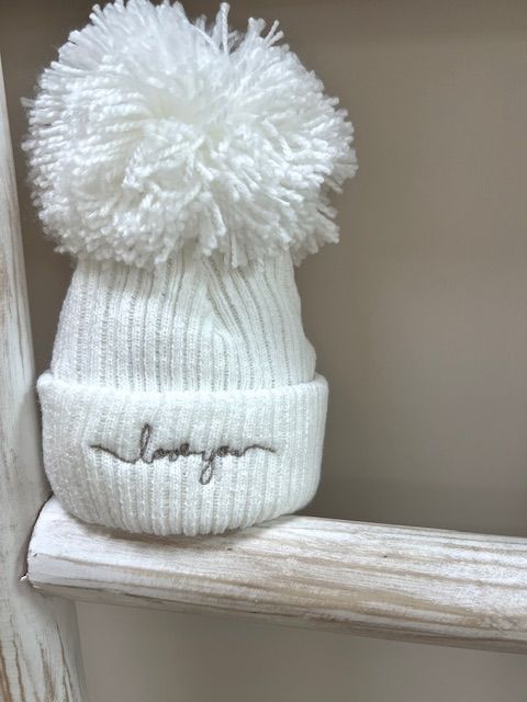 The Baby Store Love You wool pom hat displayed on rustic ladder