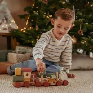 young child playing with the Little Dutch Christmas Stacking Train sitting in front of a Christmas tree